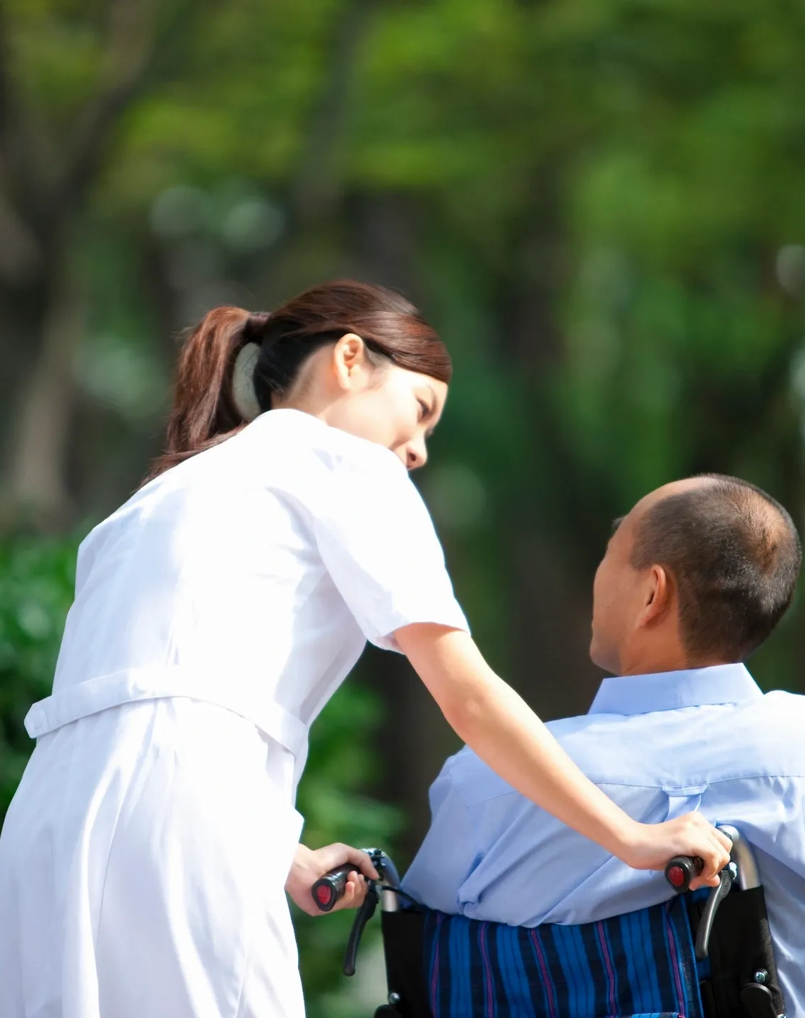 Caregiver pushing wheelchair male patient zoom in